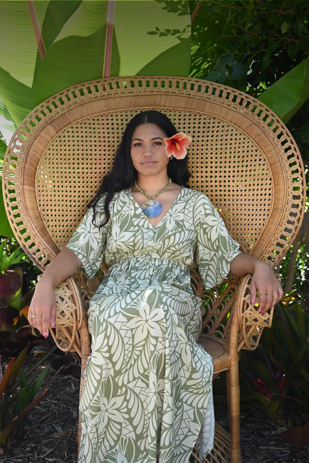 Model sitting in Cane Peacock Chair wearing the Nevaeh dress in Lagoon Sage