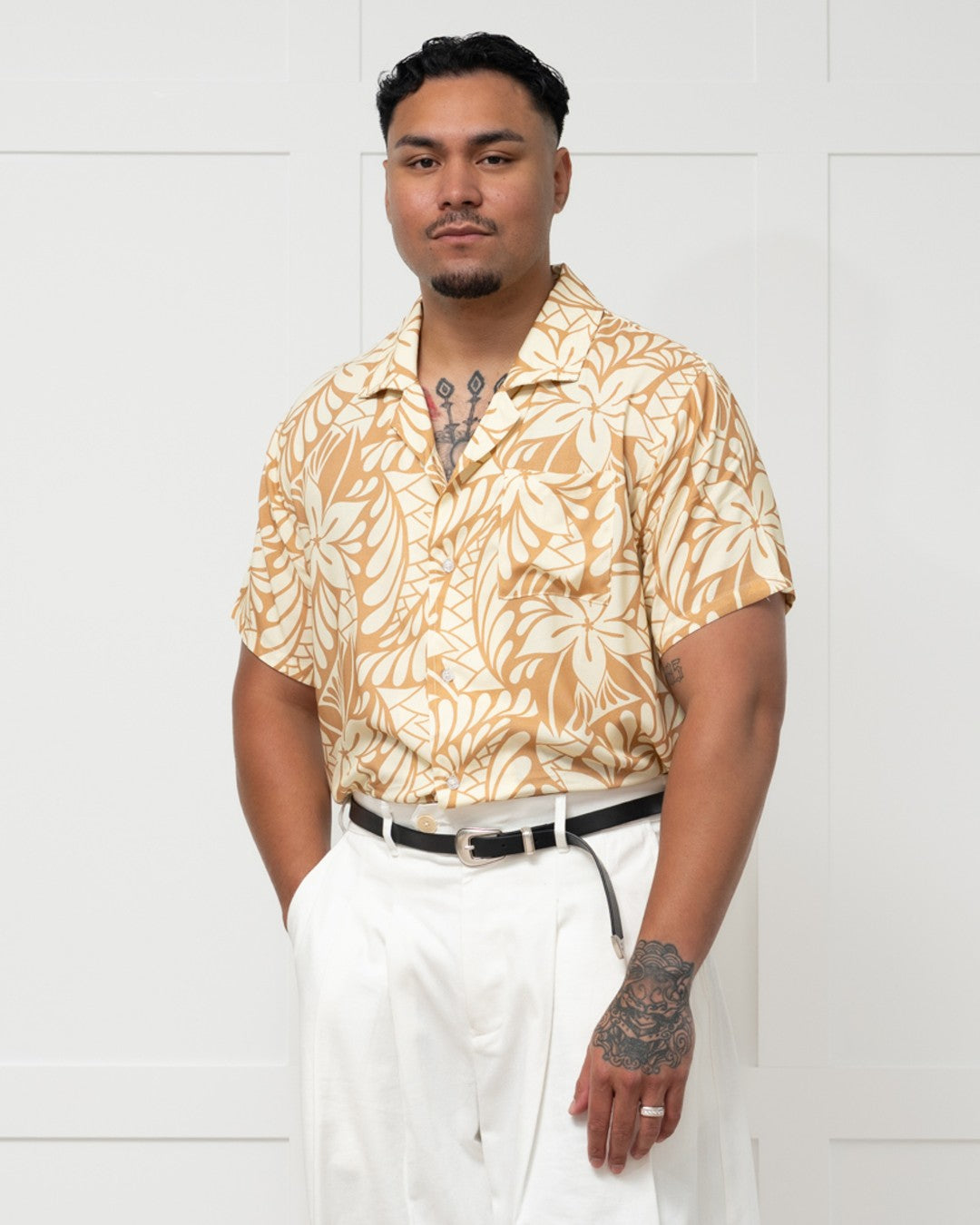 Man wearing a patterned shirt and white pants against a white background