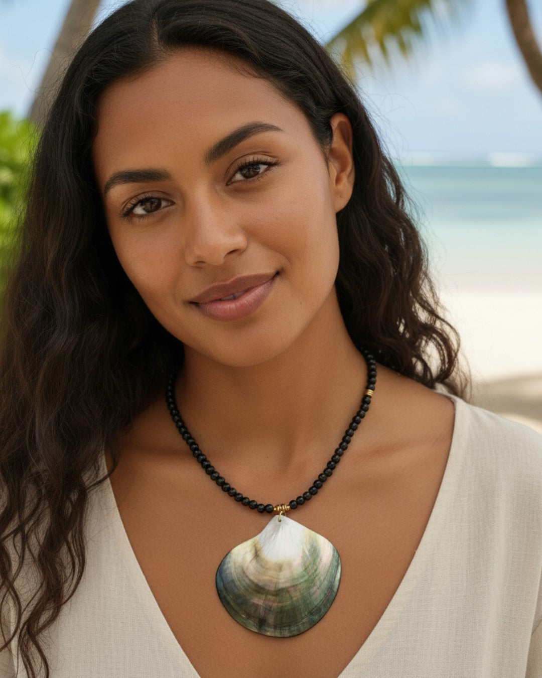 Woman wearing a large shell pendant necklace with a blurred beach background