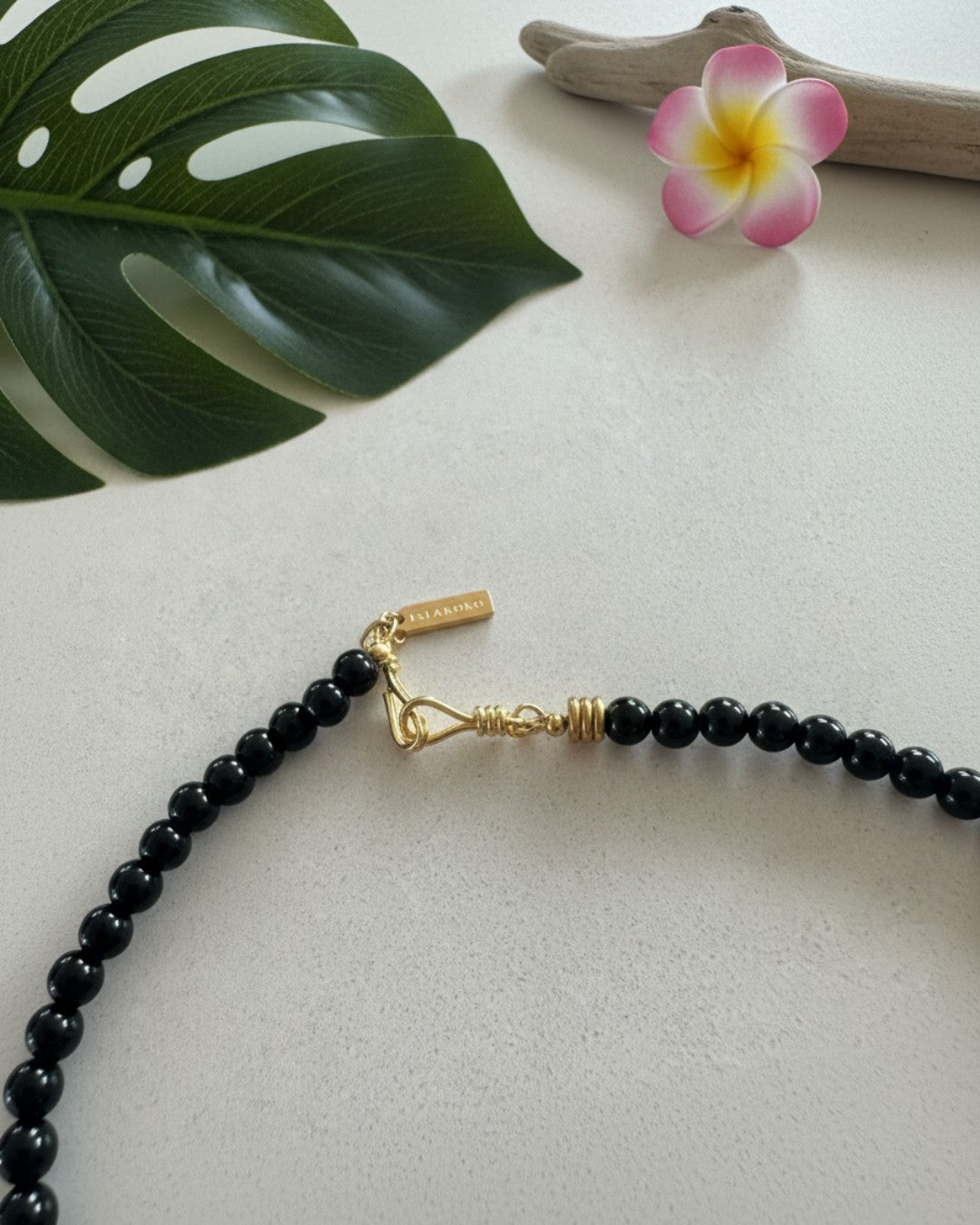 Black beaded necklace with gold clasp on a light surface with a leaf and flower in the background