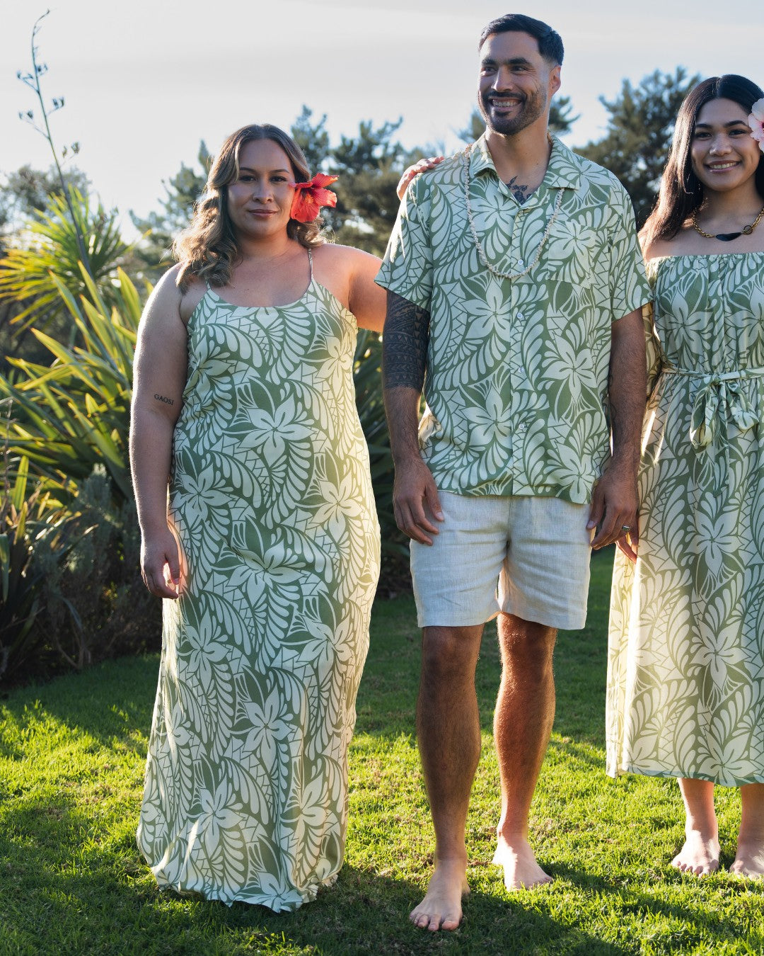 Three people wearing matching green and white island patterned outfits standing outdoors.