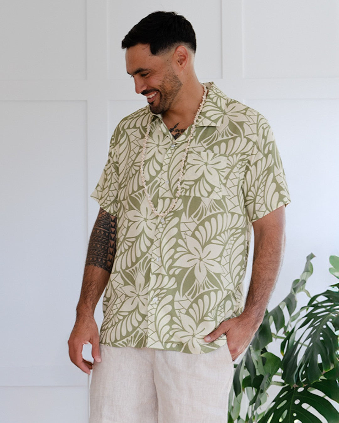 Man wearing a patterned island shirt standing in front of a white wall with plants.