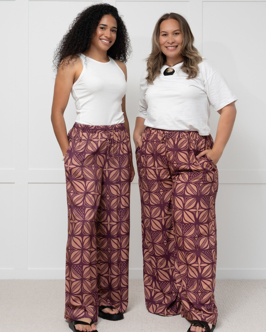 Woman wearing a white top and patterned purple island pants against a white background