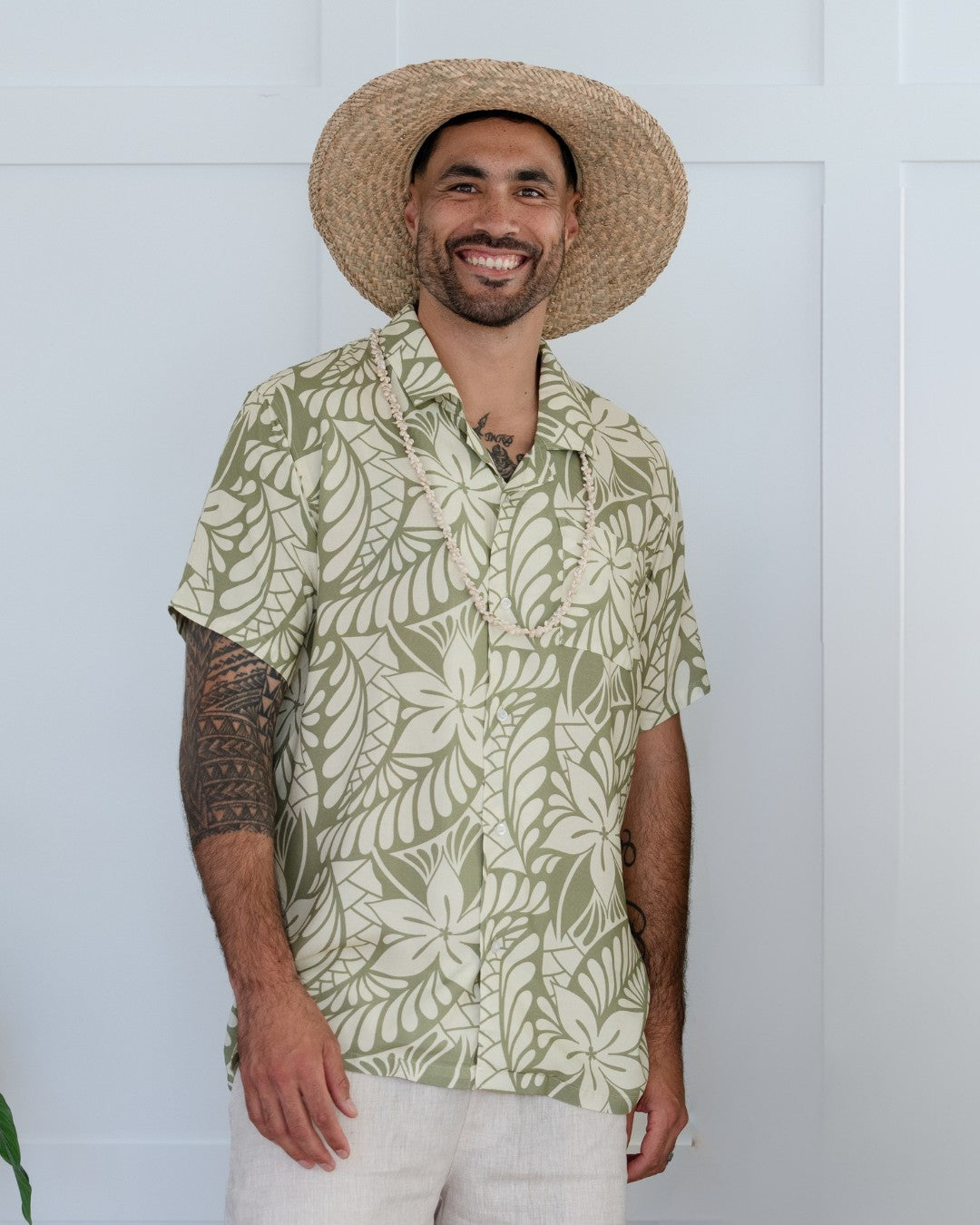 Man wearing a green leaf-patterned island shirt and straw hat against a white background