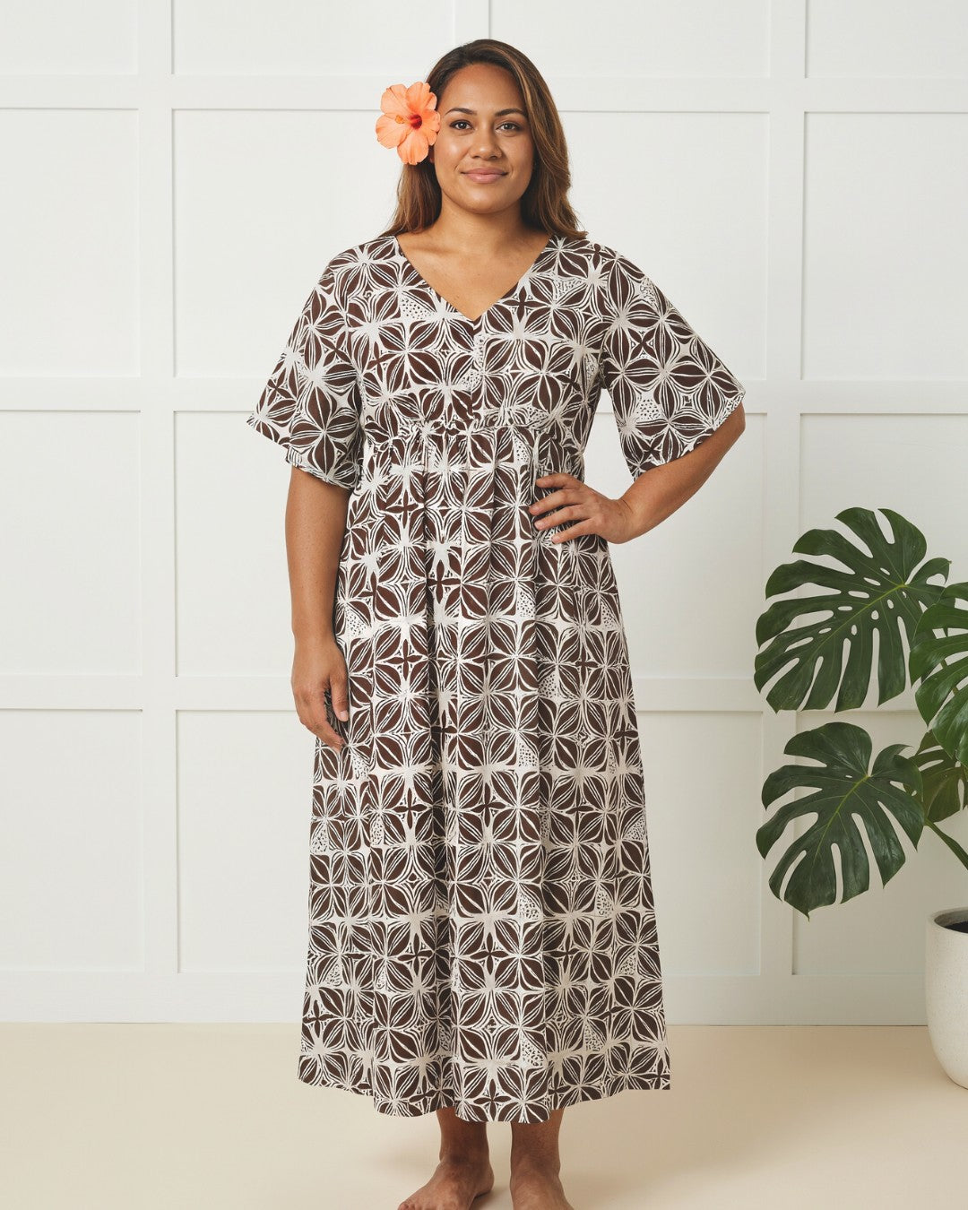 Woman wearing a patterned dress with a white wall and plant in the background