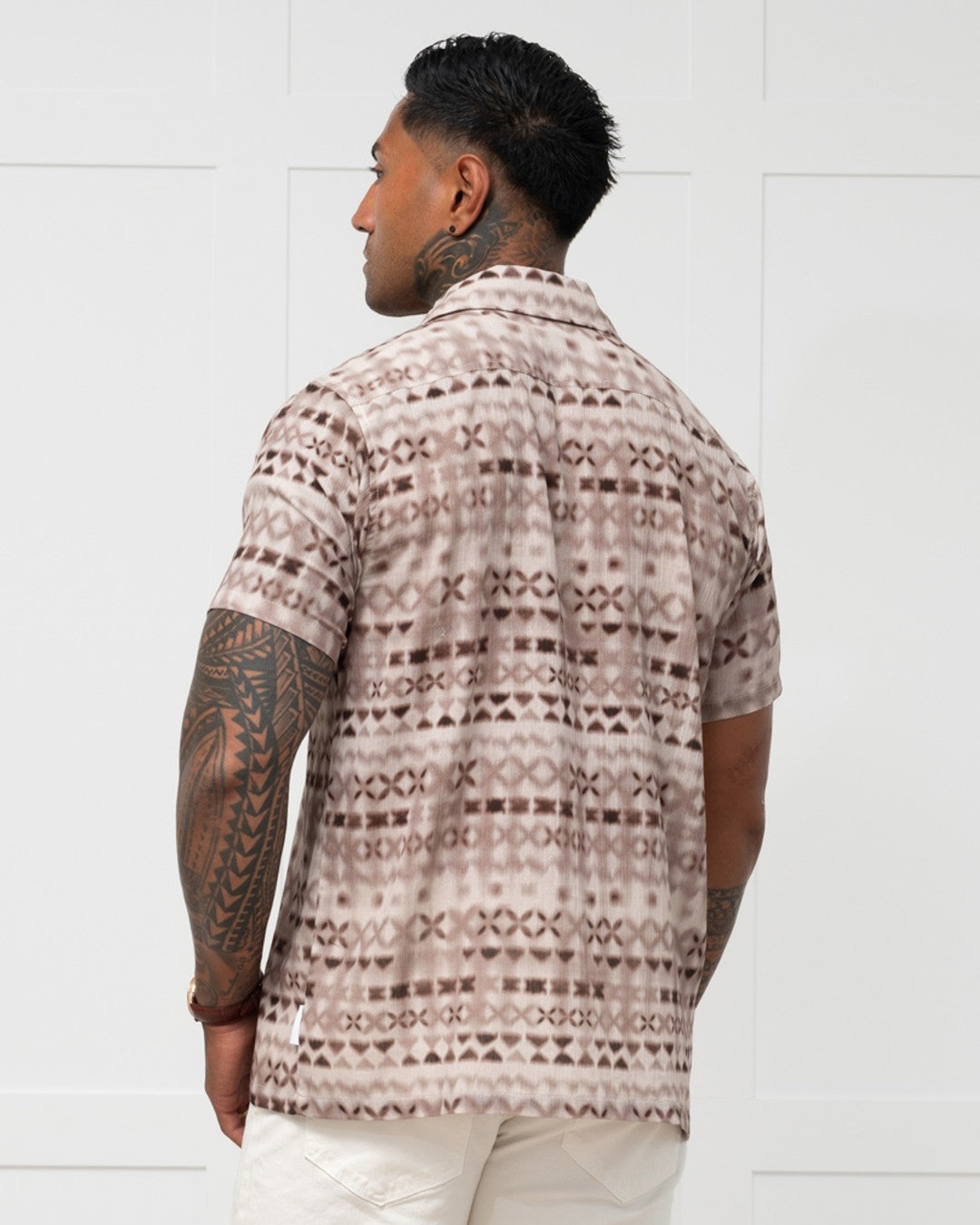 Man standing against a white wall wearing a polynesian motif mens island shirt