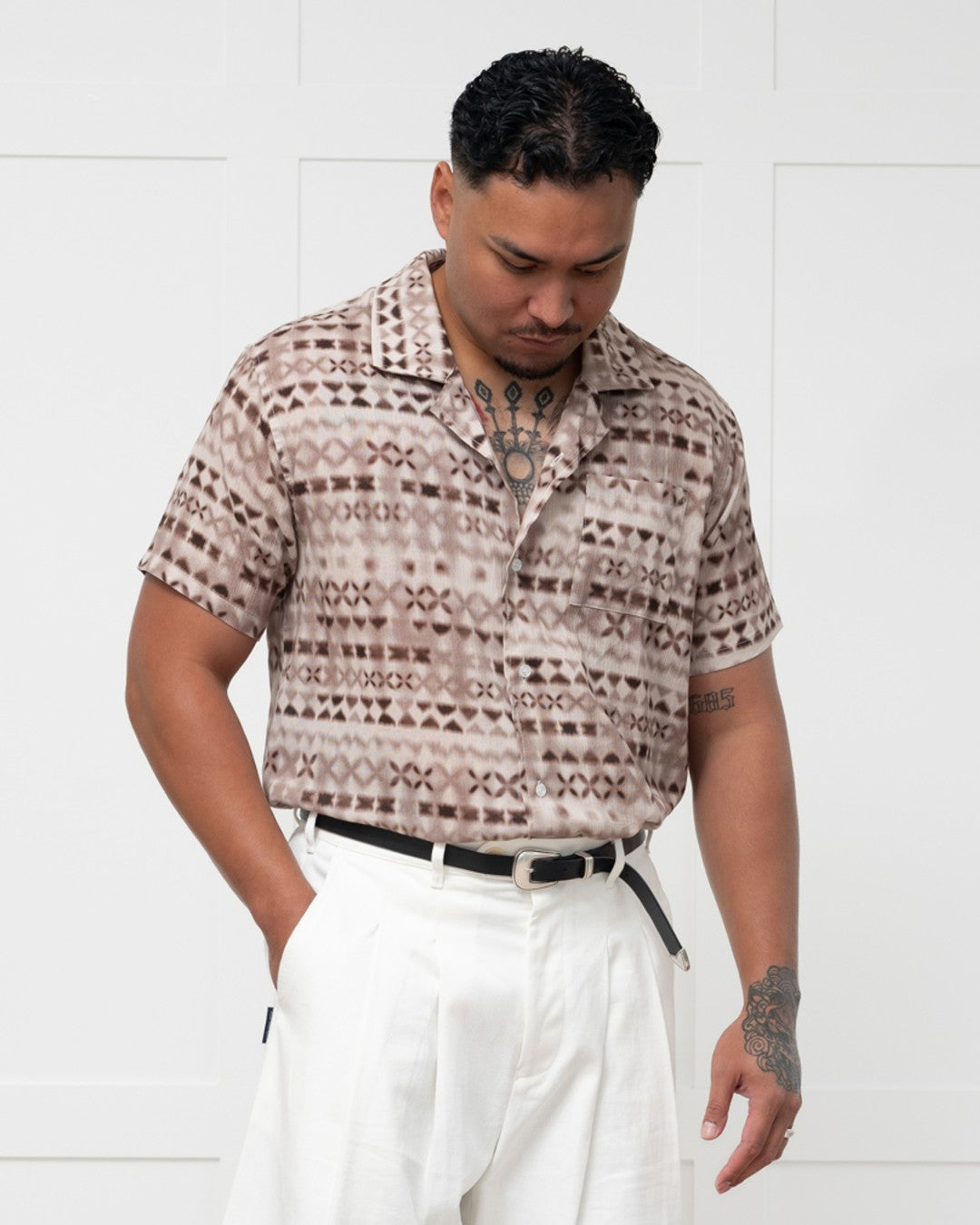 Man standing against a white wall wearing a polynesian motif mens island shirt